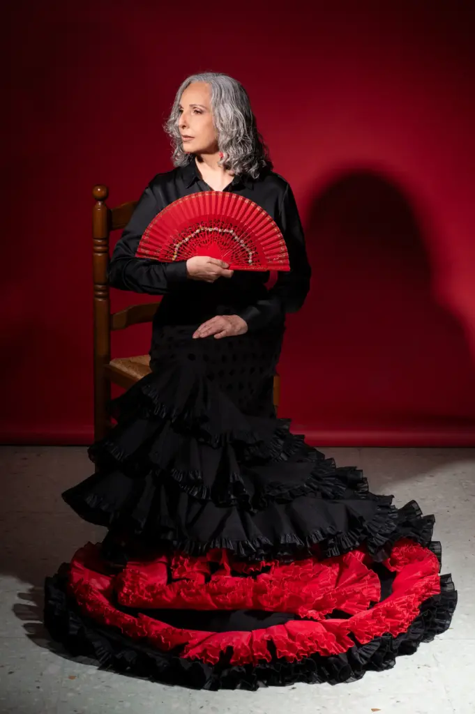 Rocío Pozo de pie con abanico rojo abierto y traje de volantes rojos sobre fondo rojo