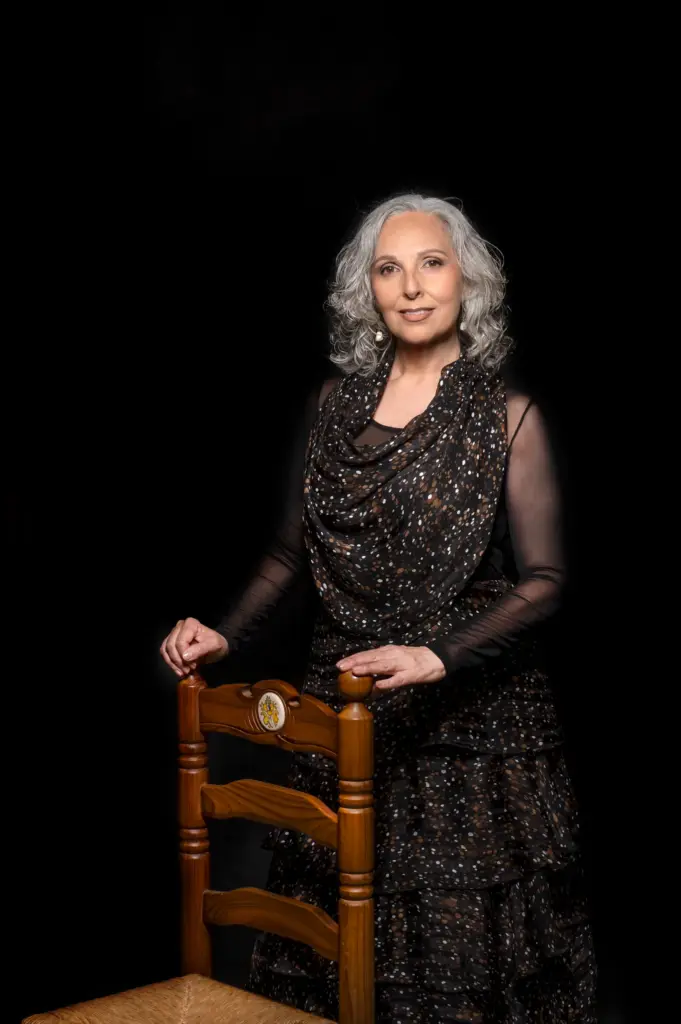 Rocío Pozo de pie, apoyada en una silla de enea, con vestido negro sobre fondo oscuro